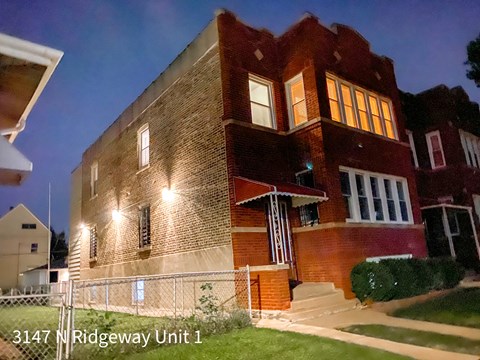 A brick building with the address 3147 N Ridgeway Unit 1 is shown at night.
