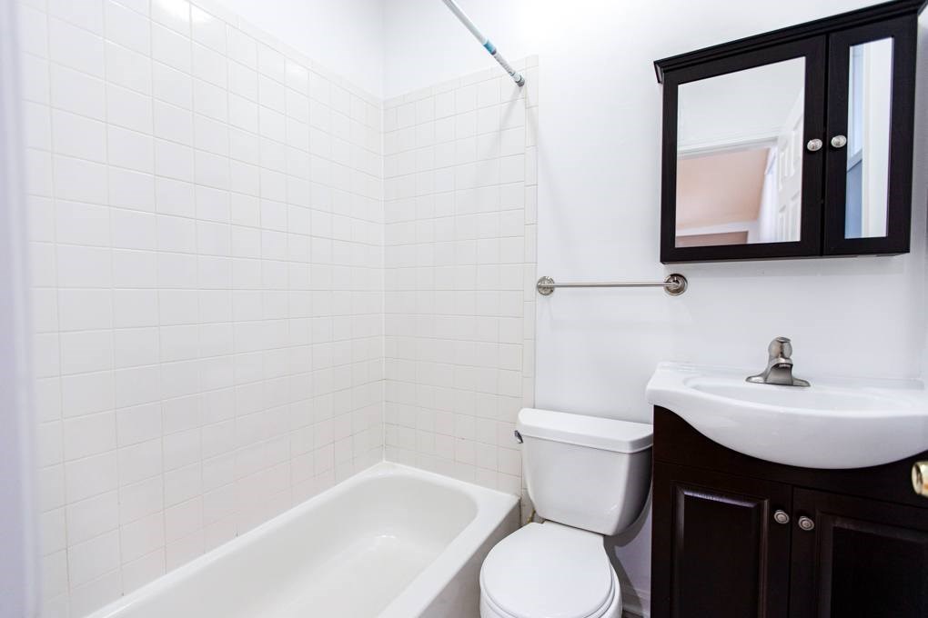 A white tiled bathroom with a white toilet, sink, and bathtub.