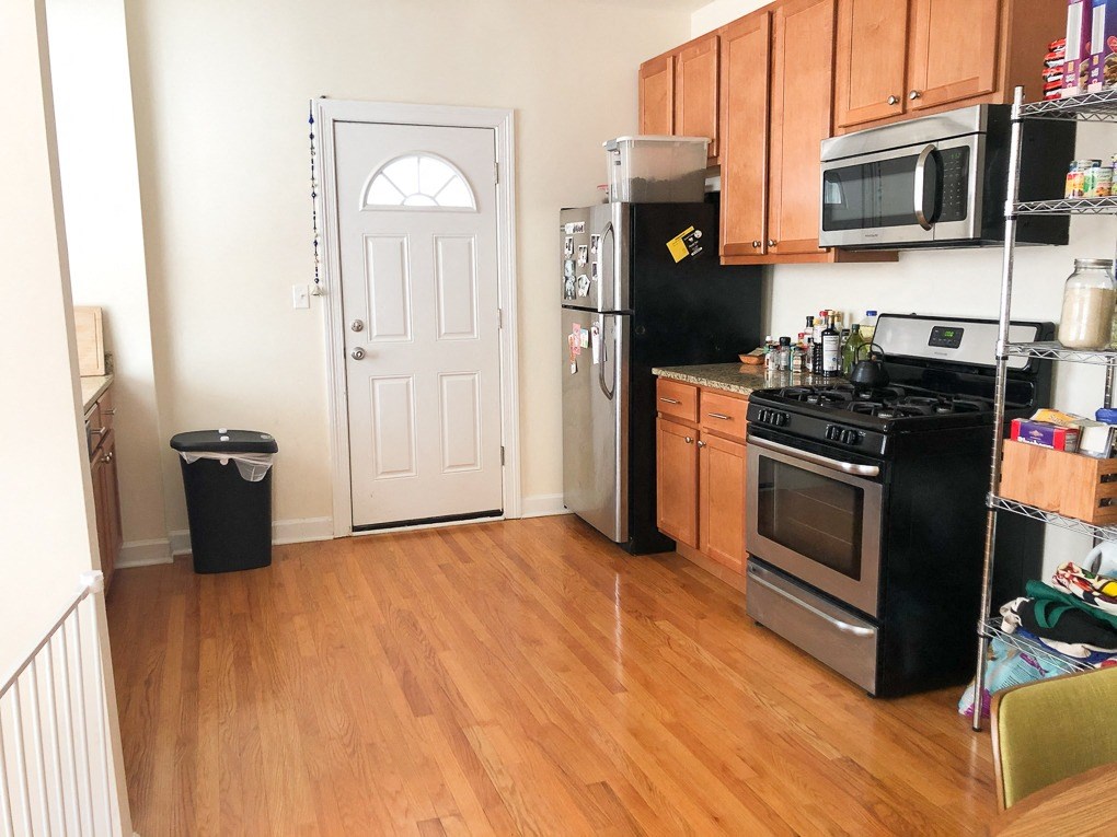 A kitchen with a black fridge and stove, wooden floors, and a white door.
