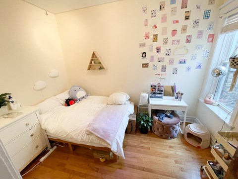 A bedroom with a bed, nightstand, and a wall covered in postcards.