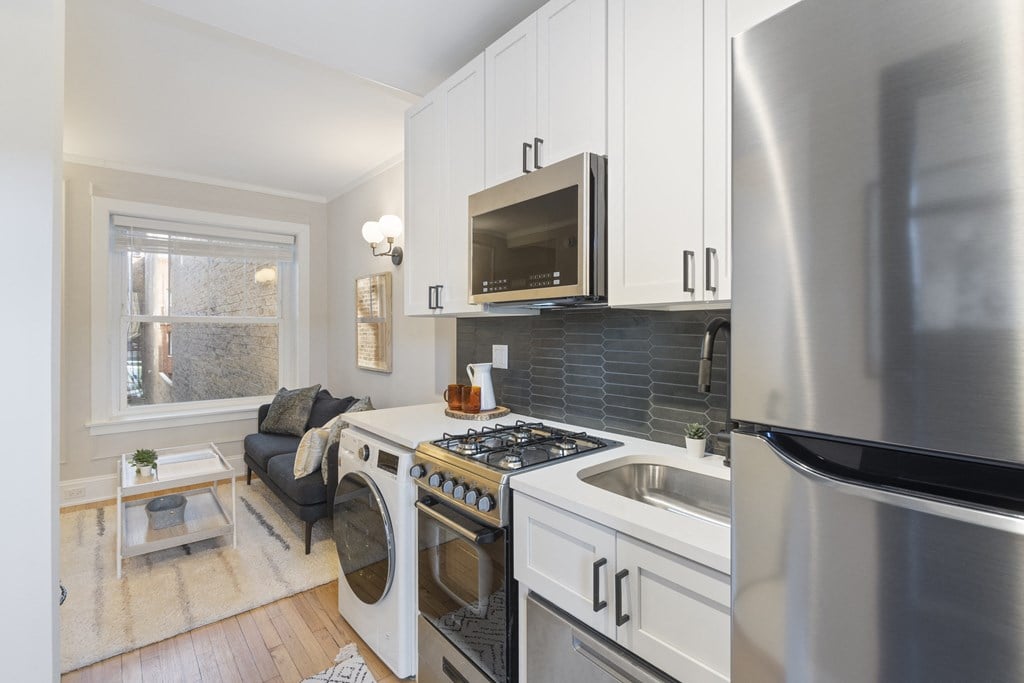 a renovated kitchen with white cabinets and appliances and a living room with a window