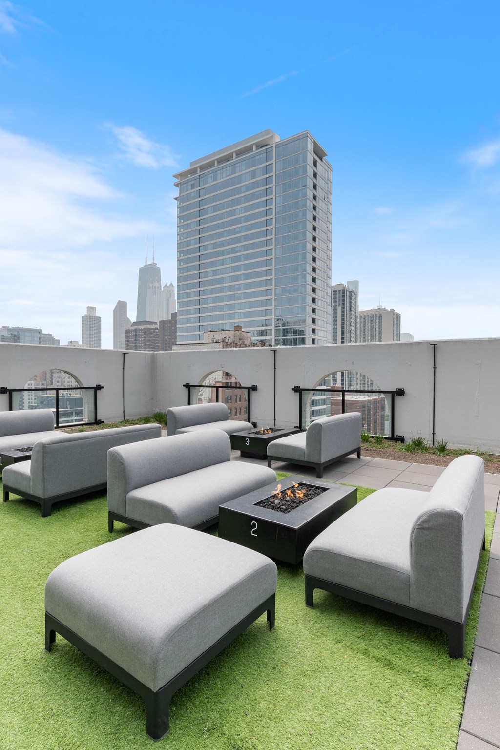 A rooftop lounge with gray comfortable couches and a fire pit with a view of Water Tower building from 1250 LaSalle