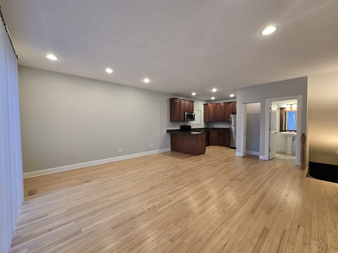A spacious room with wooden flooring and a kitchen area in the background.