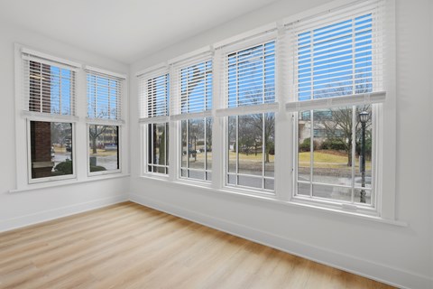 A room with white walls and wooden flooring, featuring a large window with white blinds.