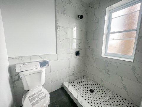 A white toilet in a bathroom with a marble wall and a window.