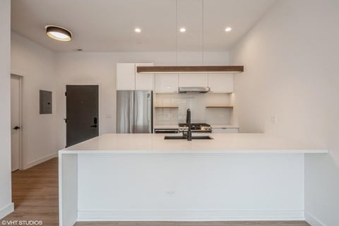 a white kitchen with a large island and a stainless steel refrigerator