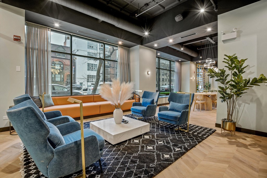 Community room at The Archer featuring comfortable blue chairs and comfortable orange sofa.