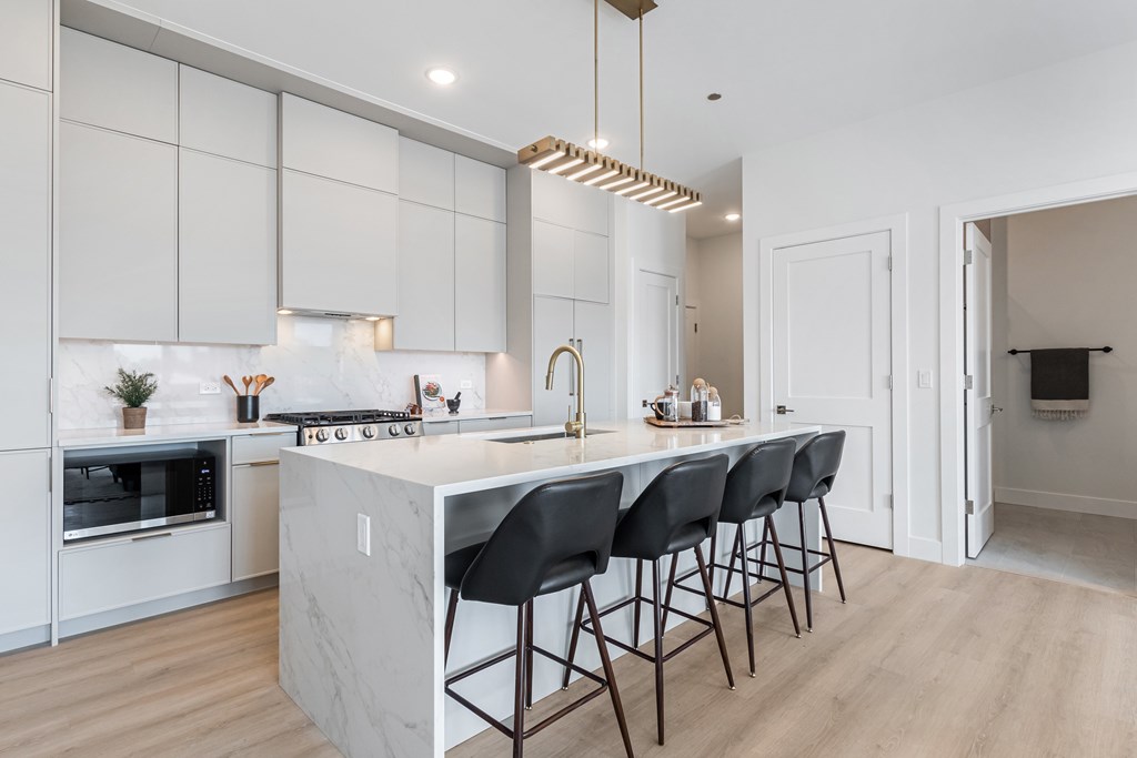 A modern kitchen with a marble island and black barstools.