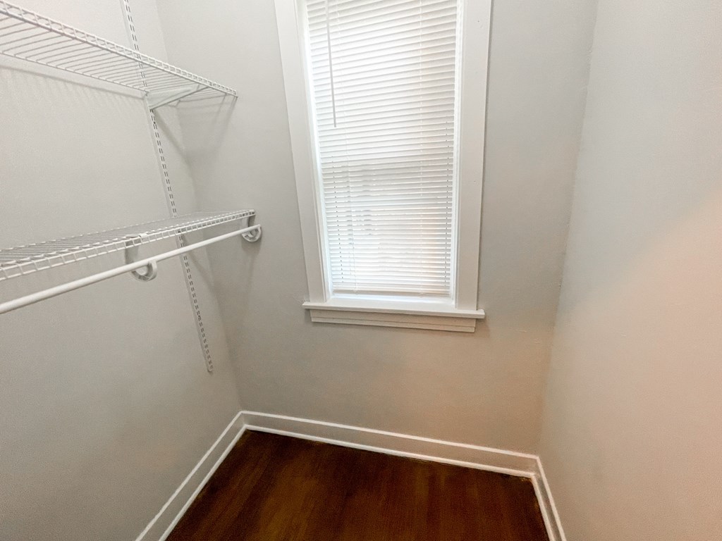 A white closet with a window and wooden floors.