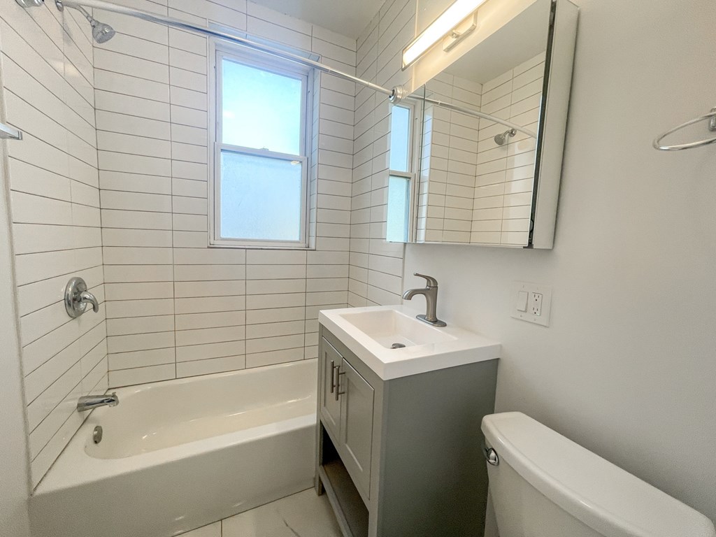 A white bathroom with a sink, tub, and mirror.