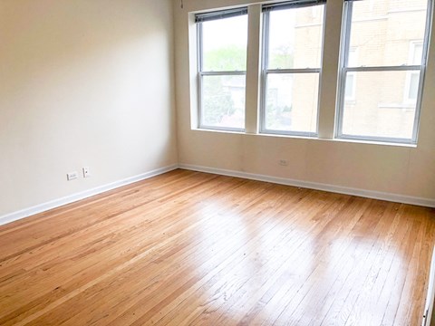 an empty room with wooden floors and three windows
