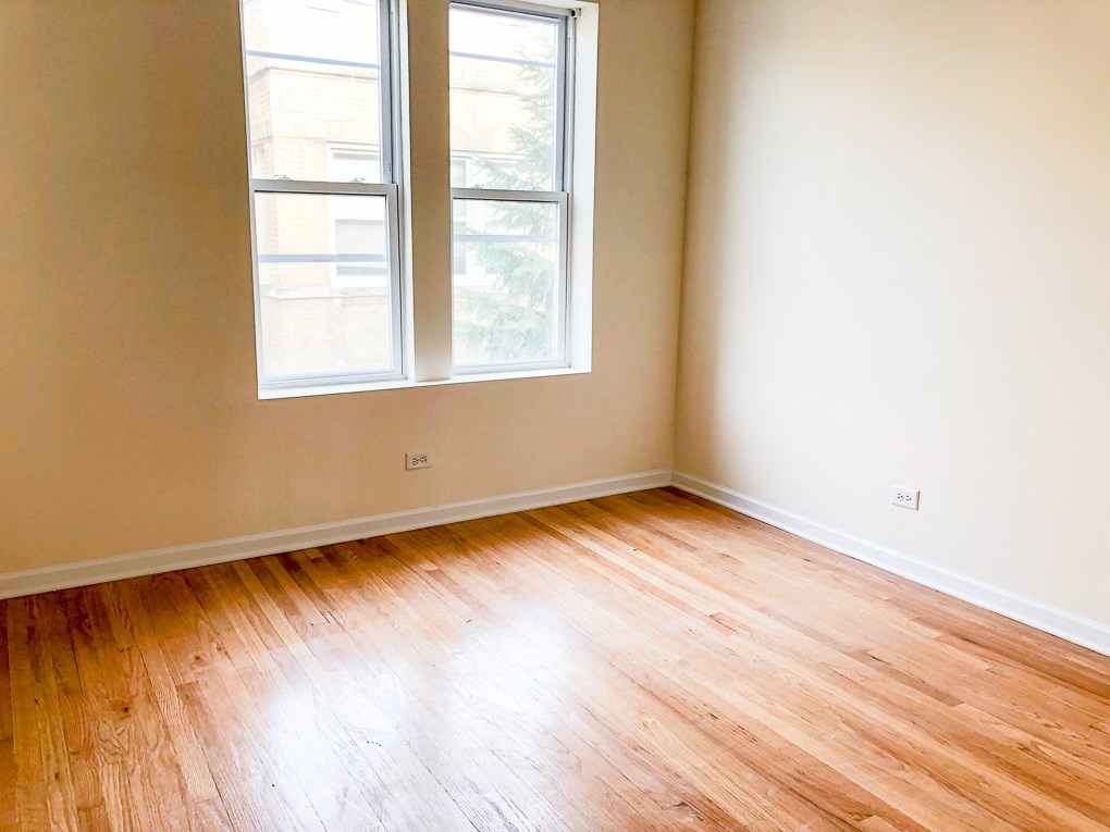 an empty room with wooden floors and two windows