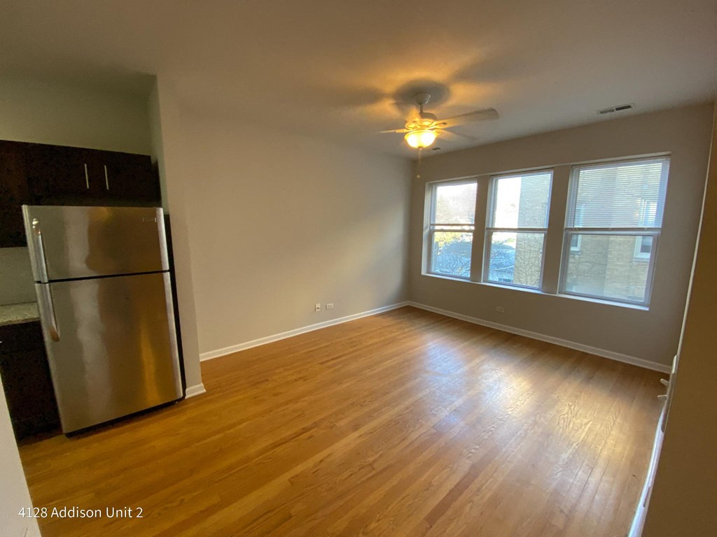 an empty living room with a refrigerator and a ceiling fan