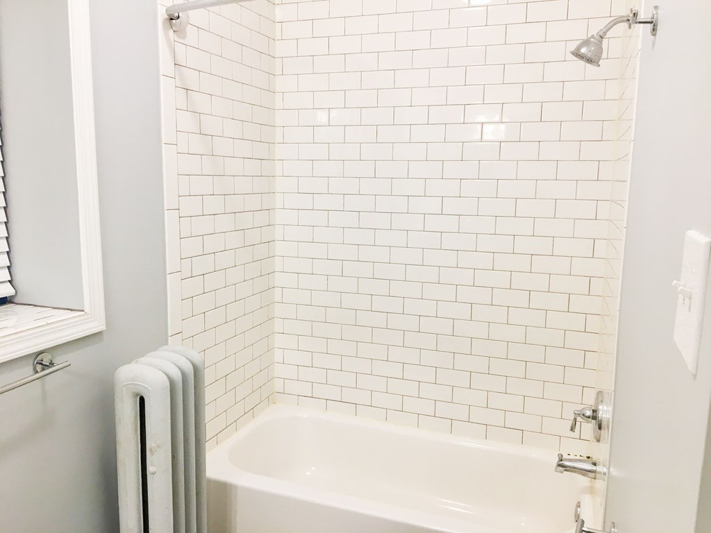A white tiled bathroom with a white tub and a white radiator.