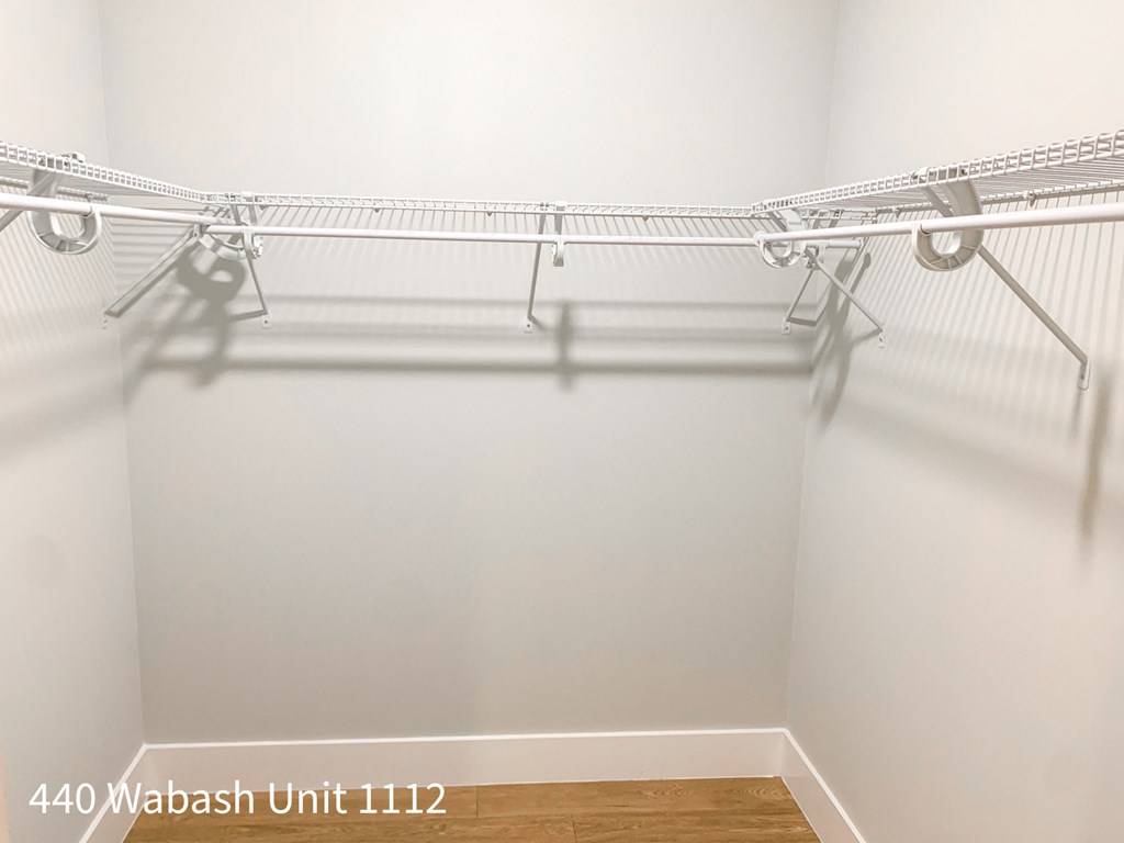 a walk in closet with white walls and a wood floor
