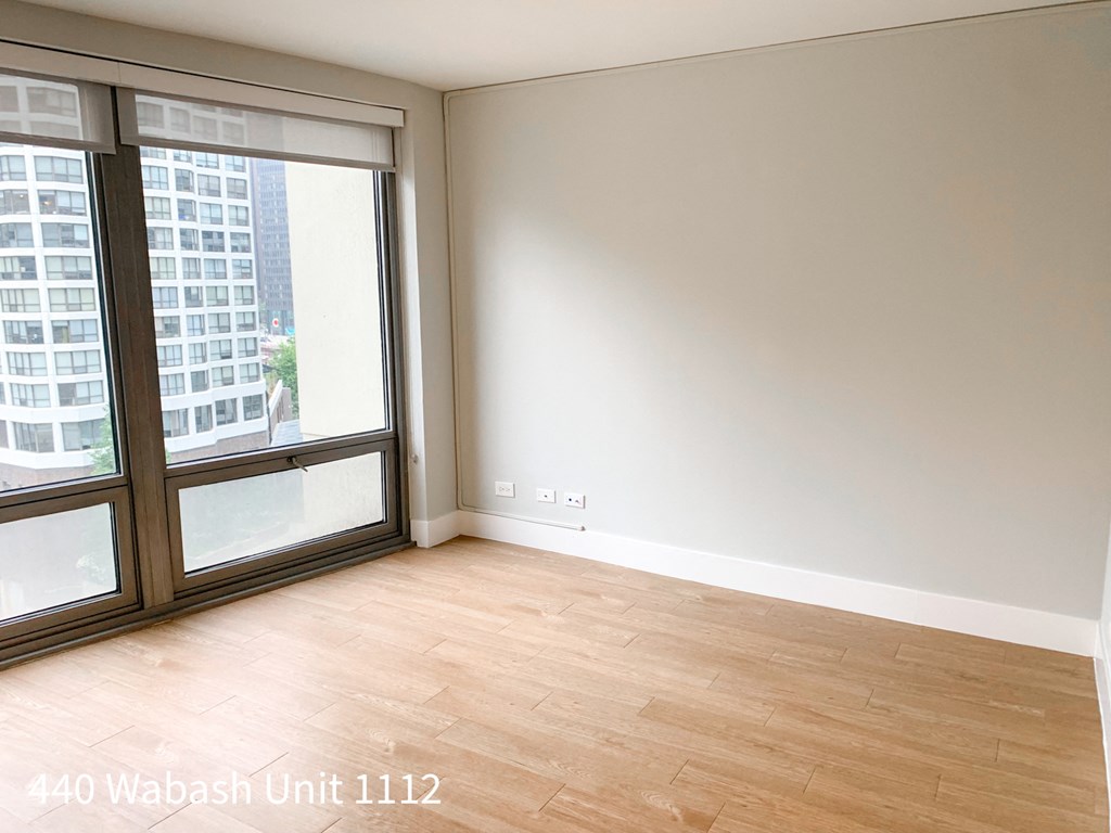 the living room of an apartment with wood flooring and large windows