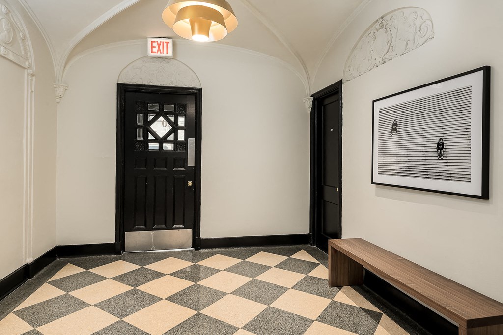 a hallway with a black door and a bench and a checkerboard floor