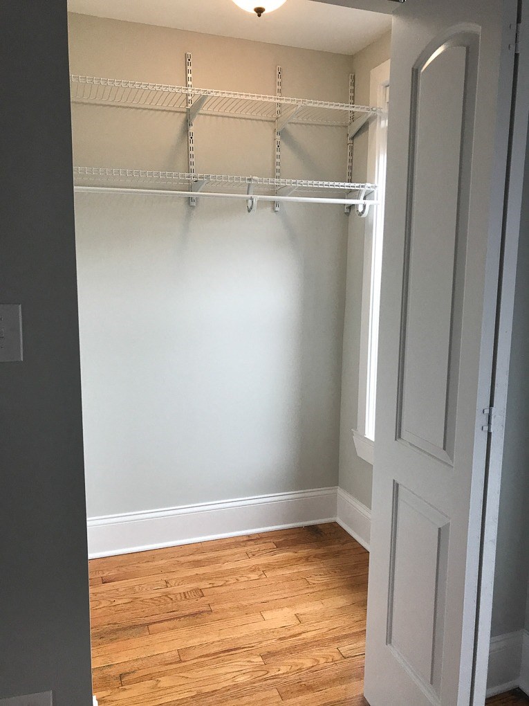 a walk in closet with white walls and a wood floor
