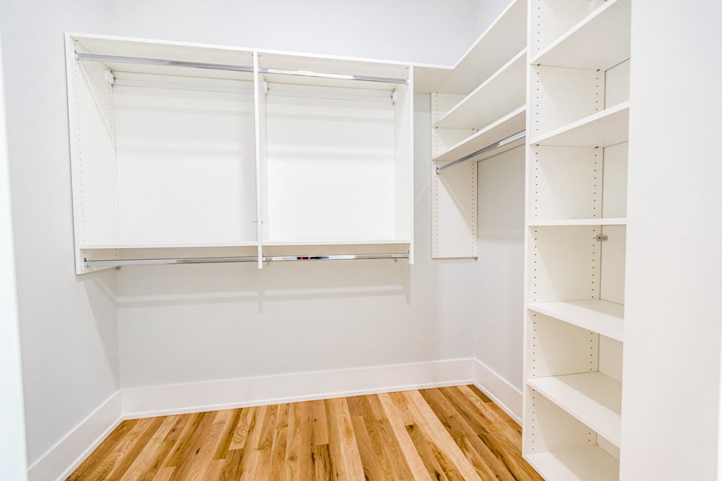 an empty closet with white shelves and a wood floor