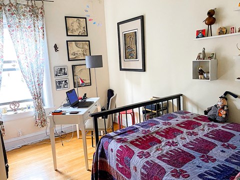 A bedroom with a bed, desk, chair, and pictures on the wall.