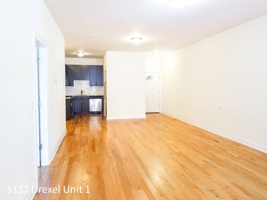 an empty living room with wood floors and a kitchen