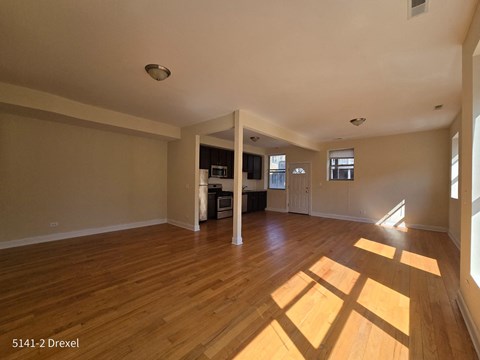 an empty living room with wood floors and a kitchen