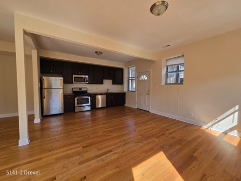 an empty living room and kitchen with wood floors and black cabinets