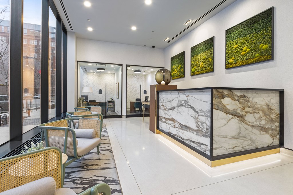 a lobby with a marble reception desk and chairs and glass doors to the management office