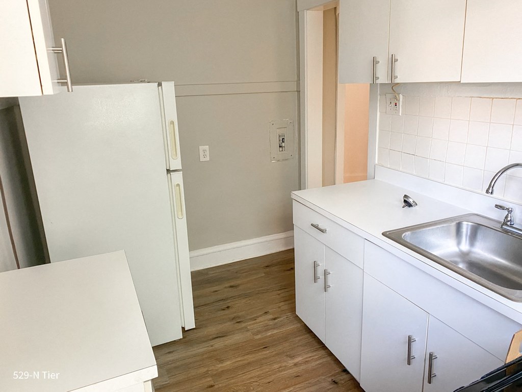 an empty kitchen with white cabinets and a sink and a refrigerator