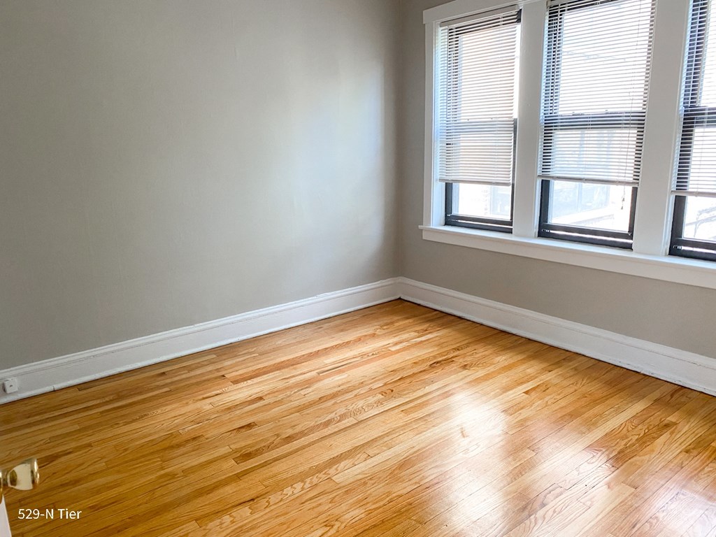 an empty room with wooden floors and three windows