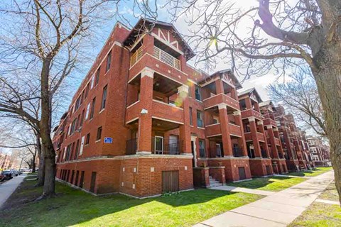 A red brick apartment building with a tree in front.