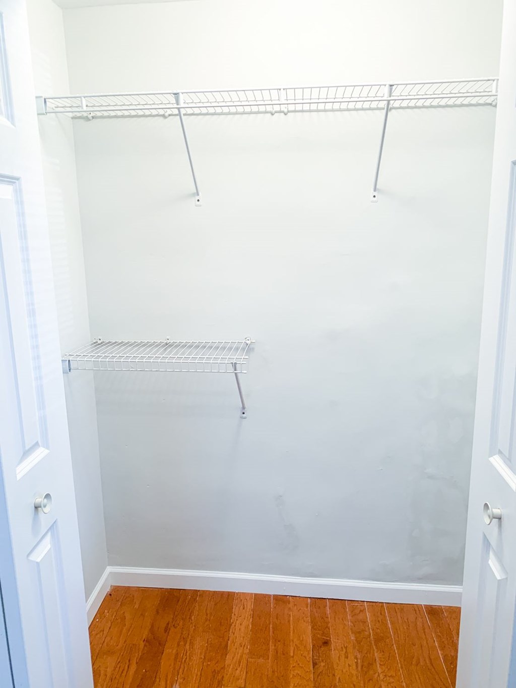 A white closet with a wooden floor and a white door.