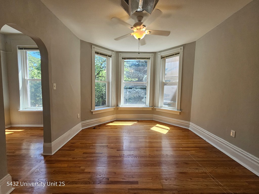 an empty living room with a ceiling fan and three windows