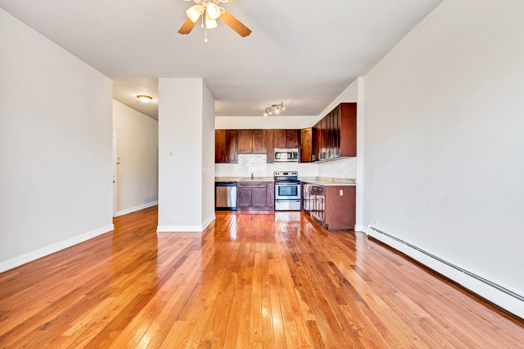 an empty living room and kitchen with wood flooring and a ceiling fan