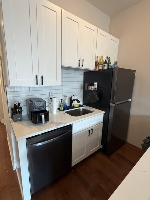 A kitchen with white cabinets and a black fridge.