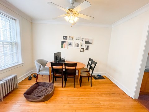 A room with a table, chairs, a dog bed, and pictures on the wall.