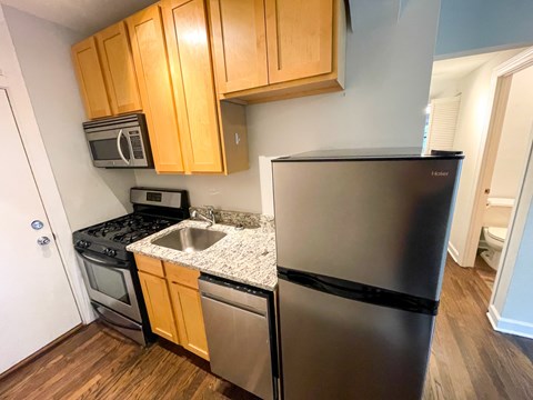 A kitchen with a black refrigerator, stainless steel sink, and wooden cabinets.