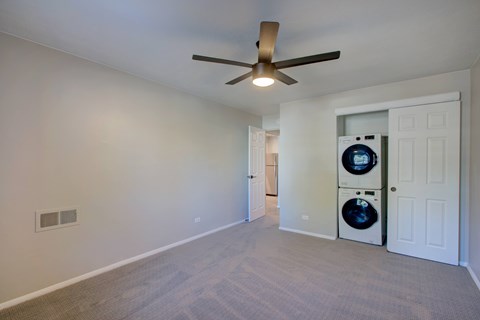A room with a ceiling fan and a washer and dryer stacked on top of each other.