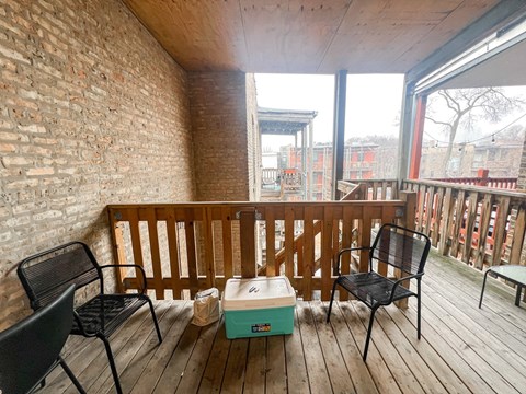 A wooden balcony with a box and chairs.