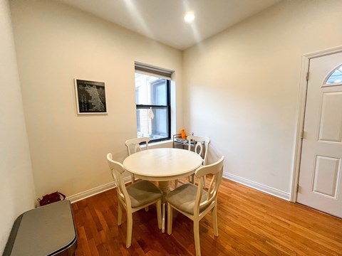 A white table with four chairs is in a room with a window.