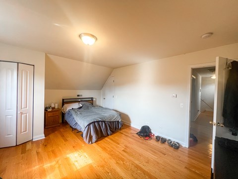A bedroom with a bed, nightstand, and a pair of shoes on the floor.