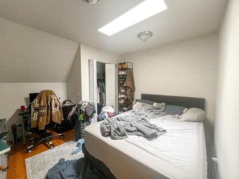 A bedroom with a bed, a chair, and a closet with clothes hanging.