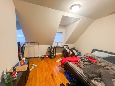 A messy bedroom with a bed, clothes, and shoes scattered about.