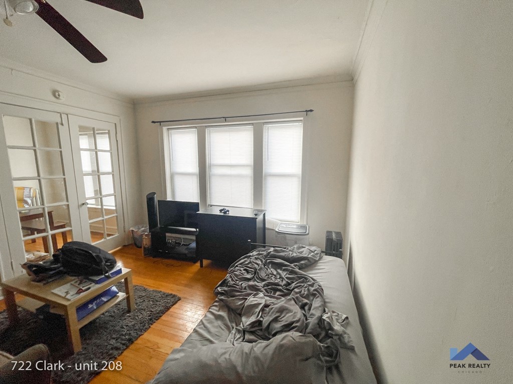 an unmade bed in a living room with a window