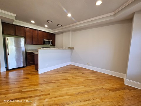 an empty living room and kitchen with wood flooring and a refrigerator