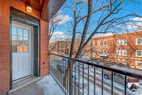 A balcony with a white door and a railing overlooking a snowy street.