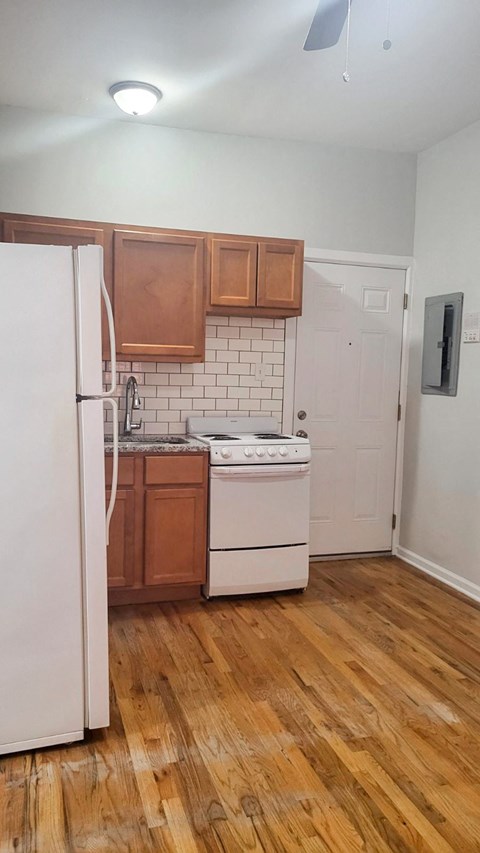 an empty kitchen with white appliances and wooden floors
