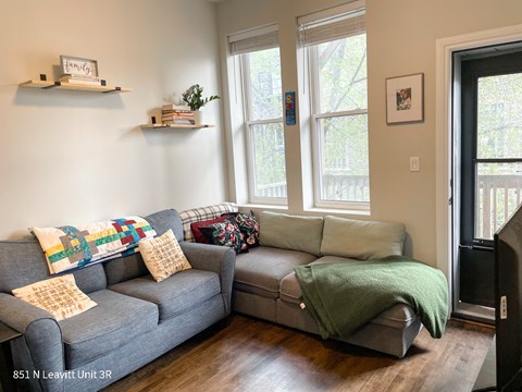 A living room with a grey couch and a green blanket on it.