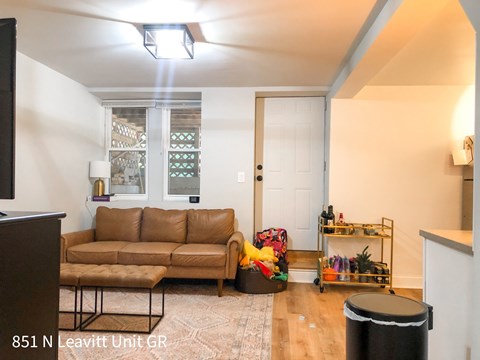 A living room with a brown couch and a black trash can.