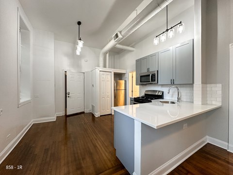 A kitchen with a white counter top and wooden floors.